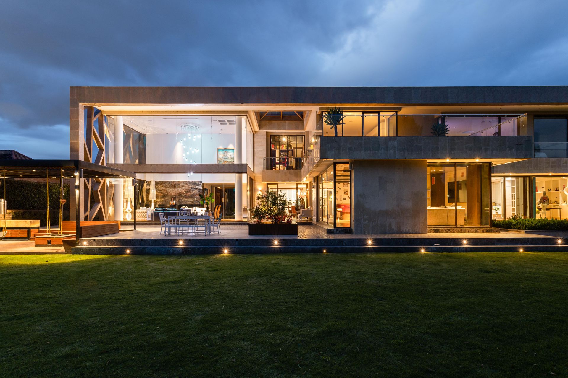 A modern glass house at dusk, its interior lit against a darkening sky.